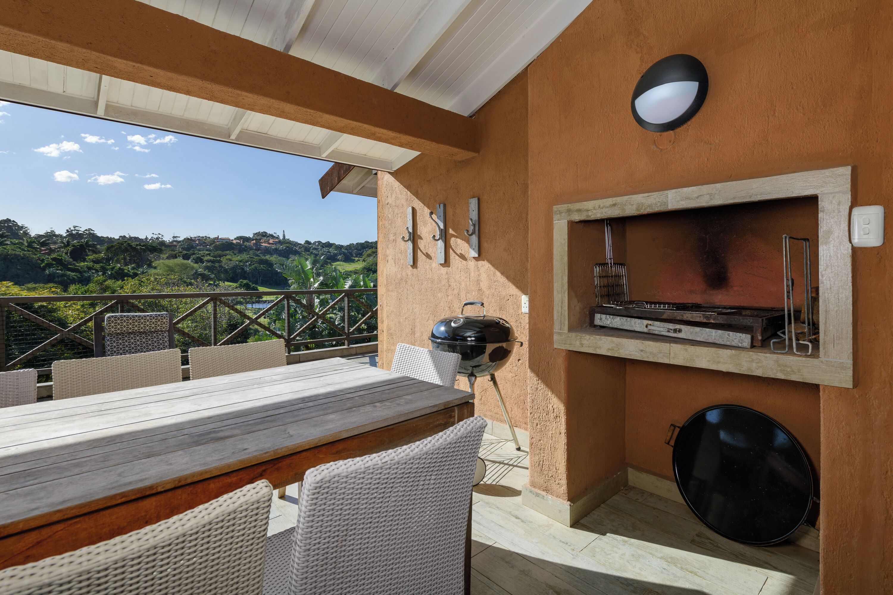 An outdoor patio with a wooden table and wicker chairs, a barbecue grill, and a built-in oven.