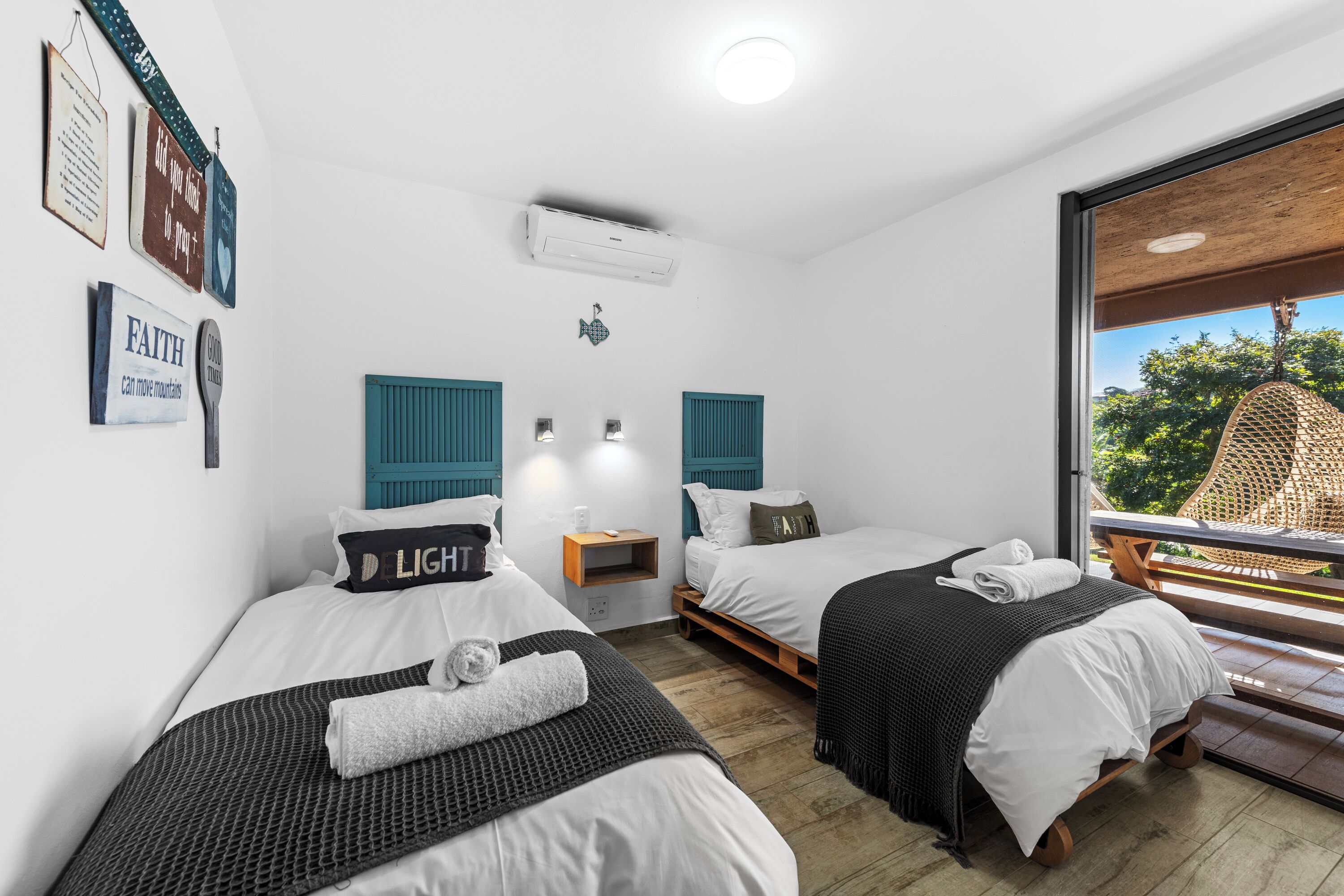A hotel room with two beds, a window with a view of greenery, and wall decorations including a sign that says "FAITH can move mountains."