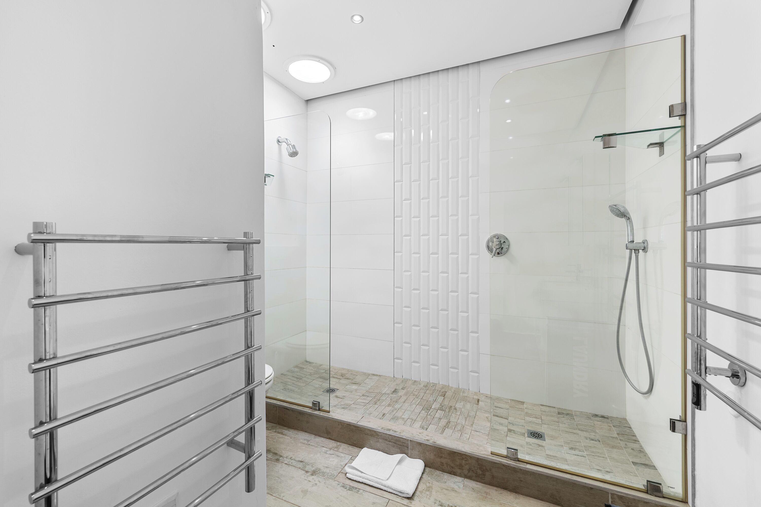 Un baño moderno con cabina de ducha de vidrio, toallero cromado y suelo de mármol.