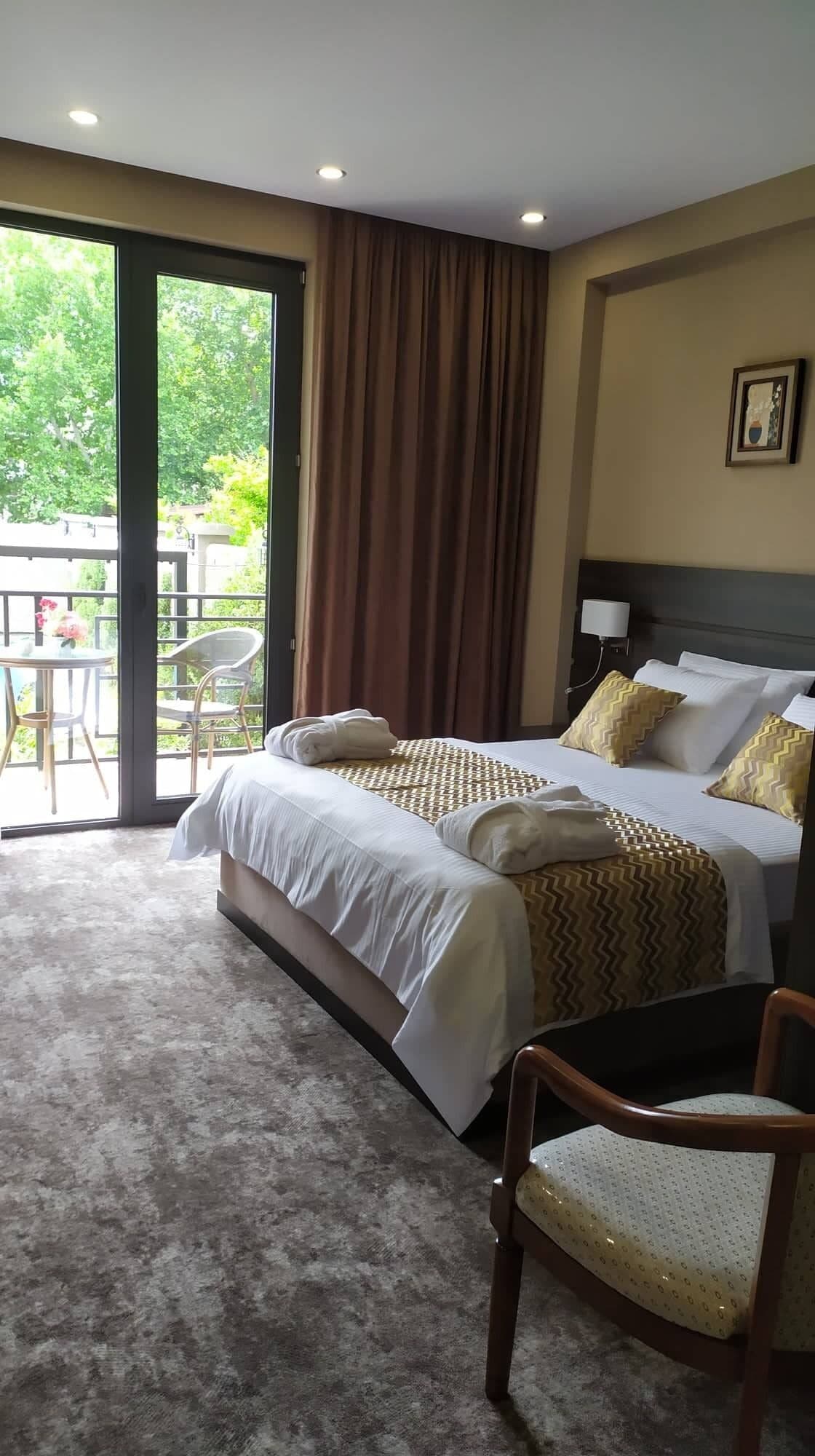 Een hotelkamer met een bed, een stoel, een tafel en uitzicht op groen buiten het raam.