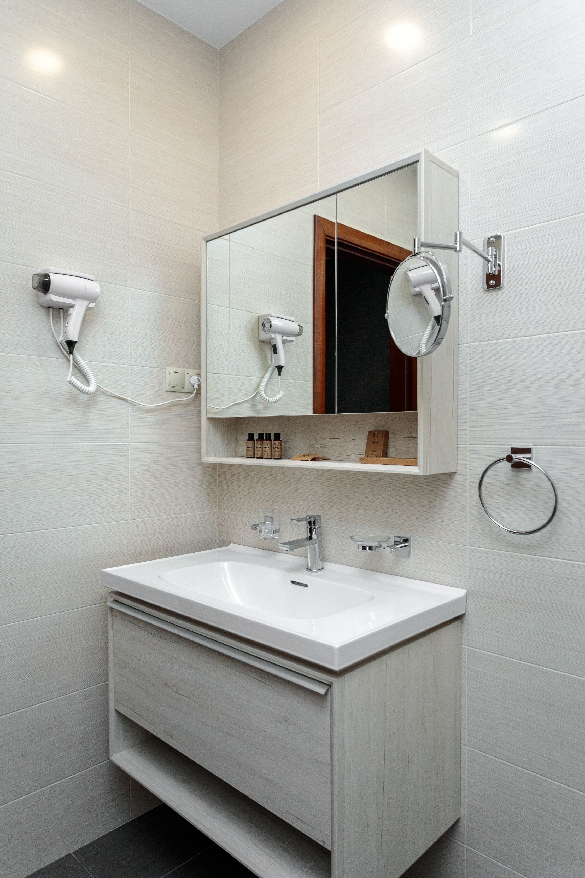 Ein modernes Badezimmer mit einem weißen Waschbecken, einem Spiegel darüber und einem an der Wand befestigten Fön.
