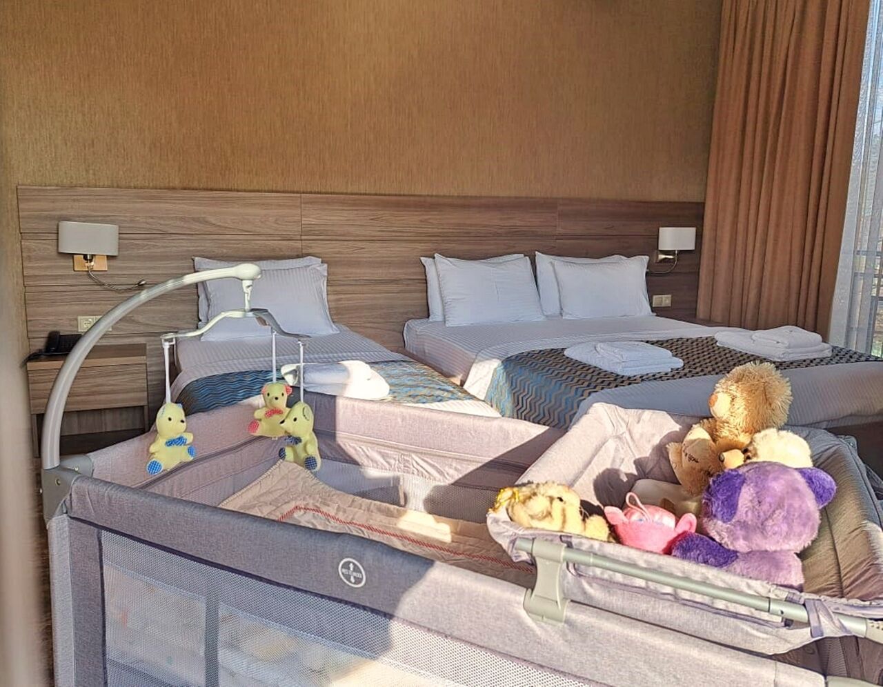 A hotel room with two beds, a crib, and a variety of stuffed toys.