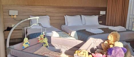A hotel room with two beds, a crib, and a variety of stuffed toys.