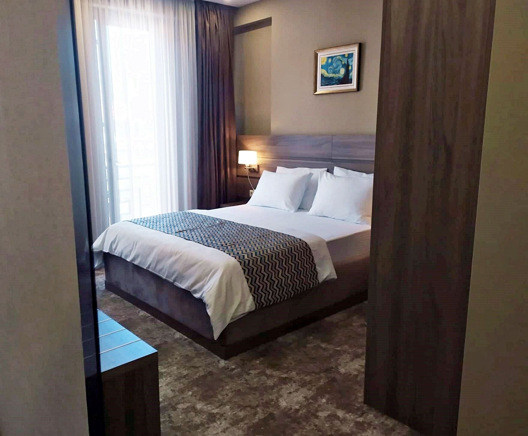 Ein Hotelzimmer mit einem Bett, einem Nachttisch, einer Lampe und einem Gemälde an der Wand.