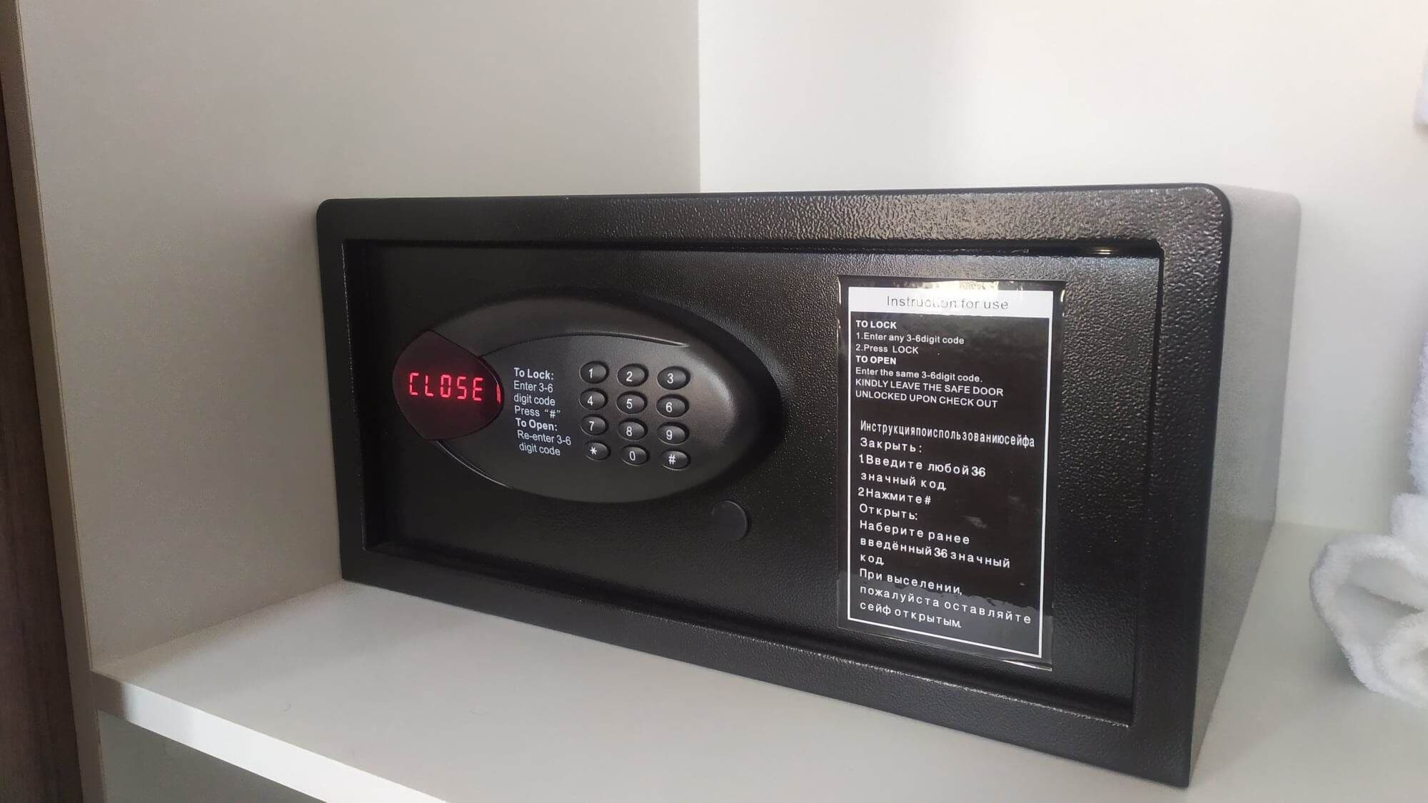 Ein digitaler Safes mit Tastatur und Sperrbildschirm, der "CLOSE" anzeigt. Eine an dem Safe angebrachte Beschriftung enthält Gebrauchsanweisungen.
