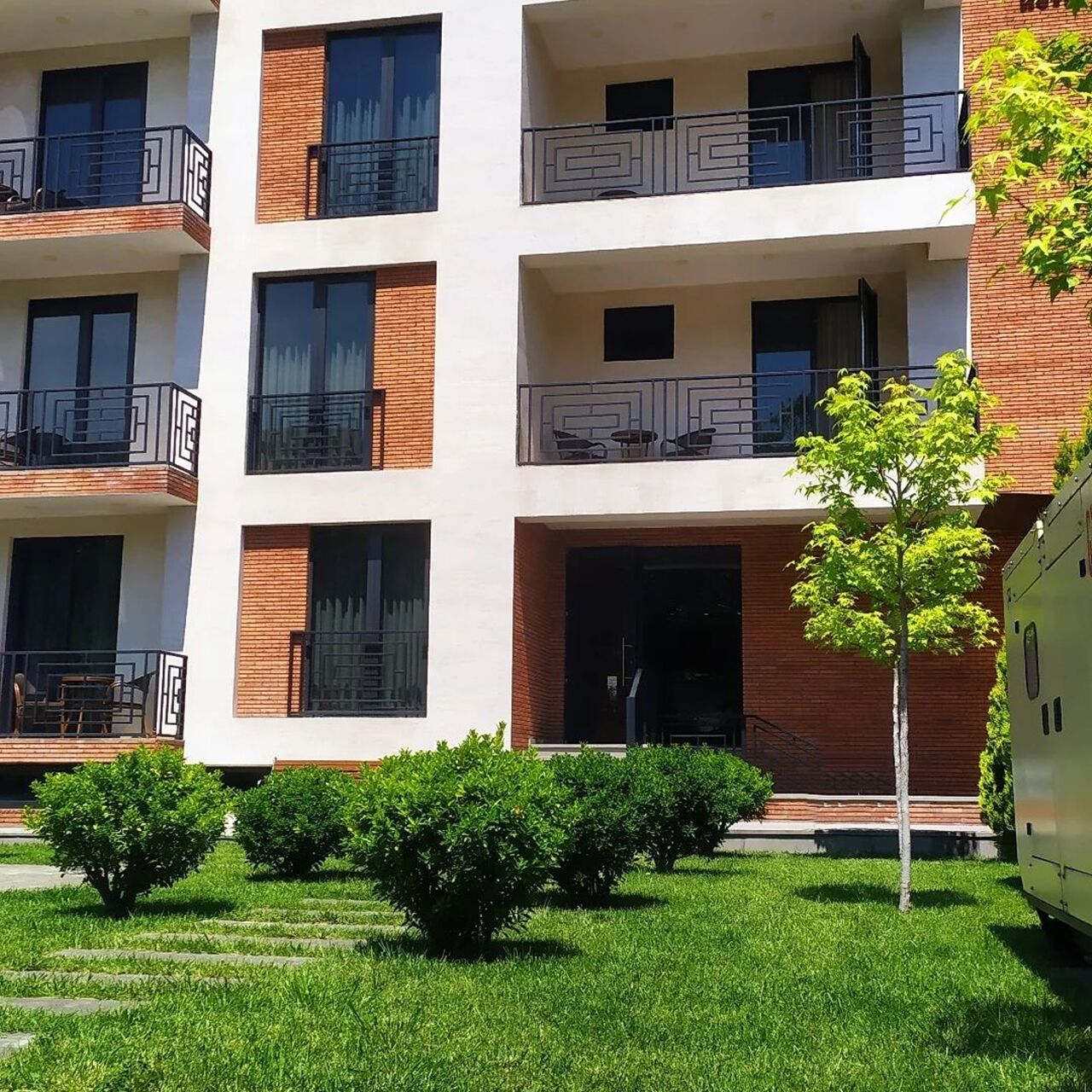 A multi-story building with balconies, a small tree, and a well-maintained lawn.