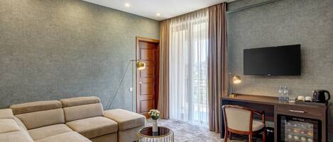 A modern hotel room with a sofa, a desk, a television, and a minibar.