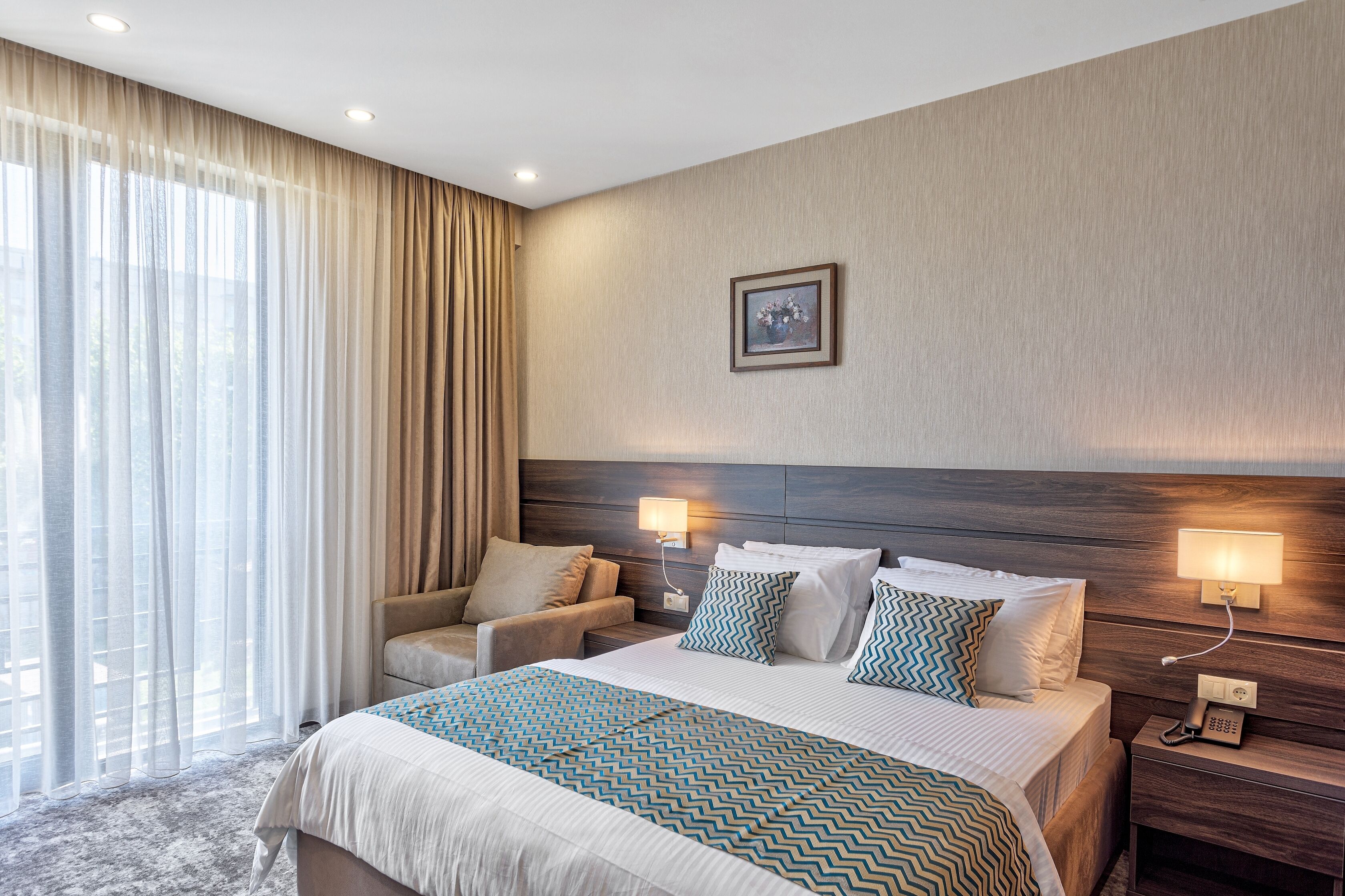Una habitación de hotel con una cama grande, un sofá, una mesita de noche con un teléfono y una lámpara de pared.