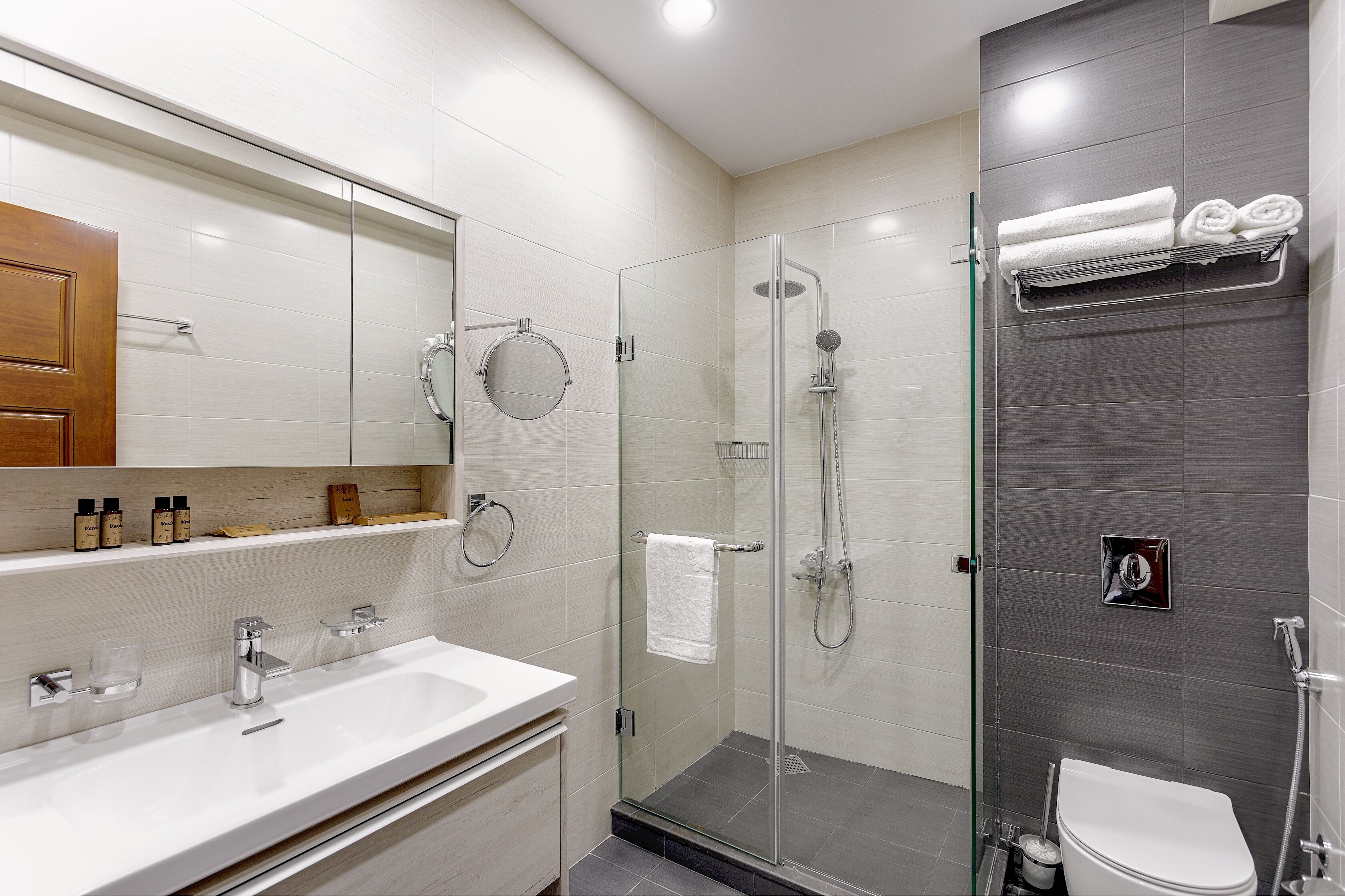Een moderne badkamer met een douchecabine van glas, een witte wastafel en een toilet.