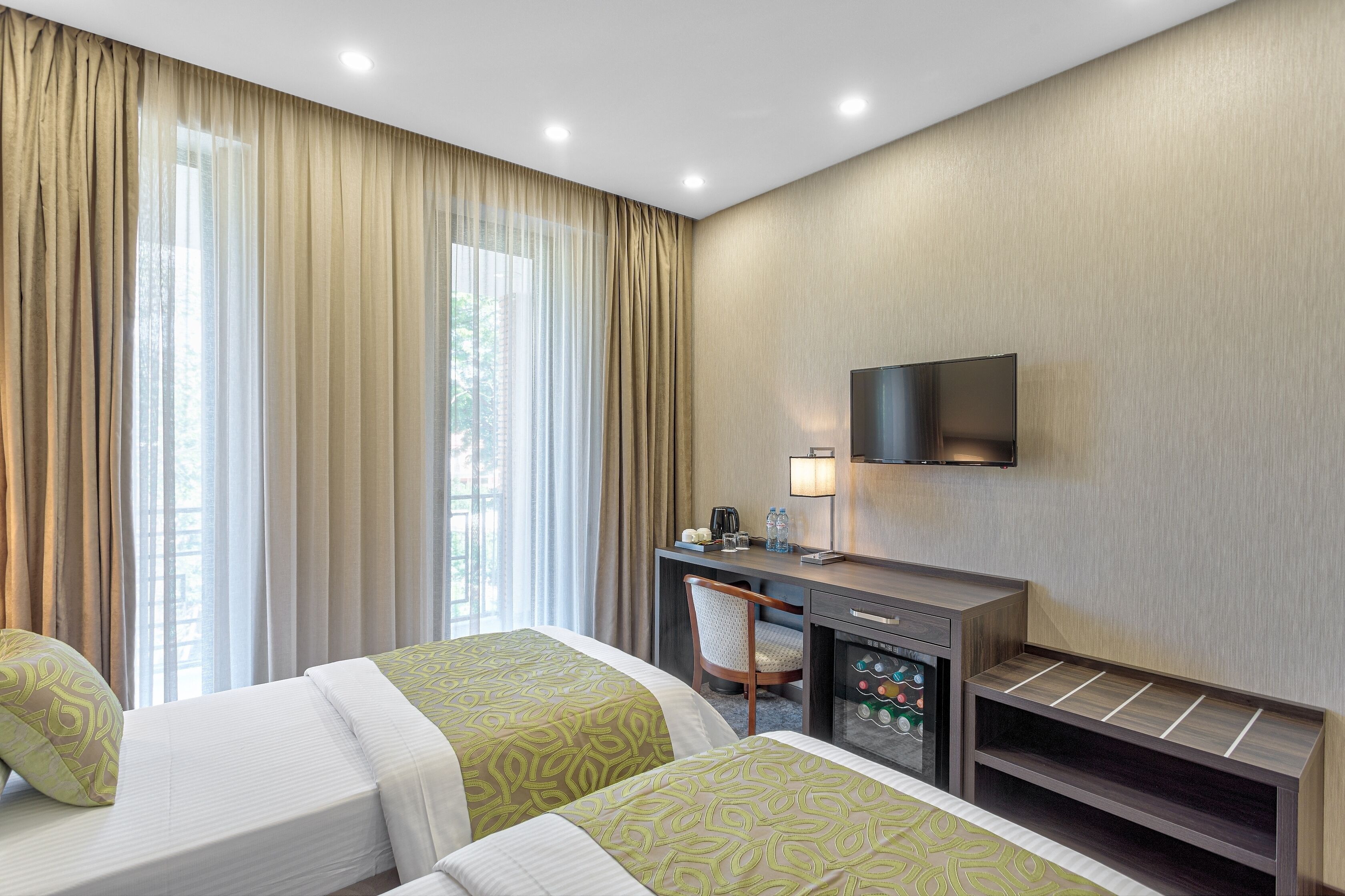 A hotel room with two beds, a desk with a chair, a television mounted on the wall, and a minibar.