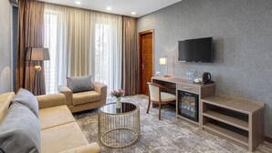 A hotel room with a sofa, a round coffee table, a desk with a computer, a TV, and a minibar. - Vinum Hotel (Tbilisi)
