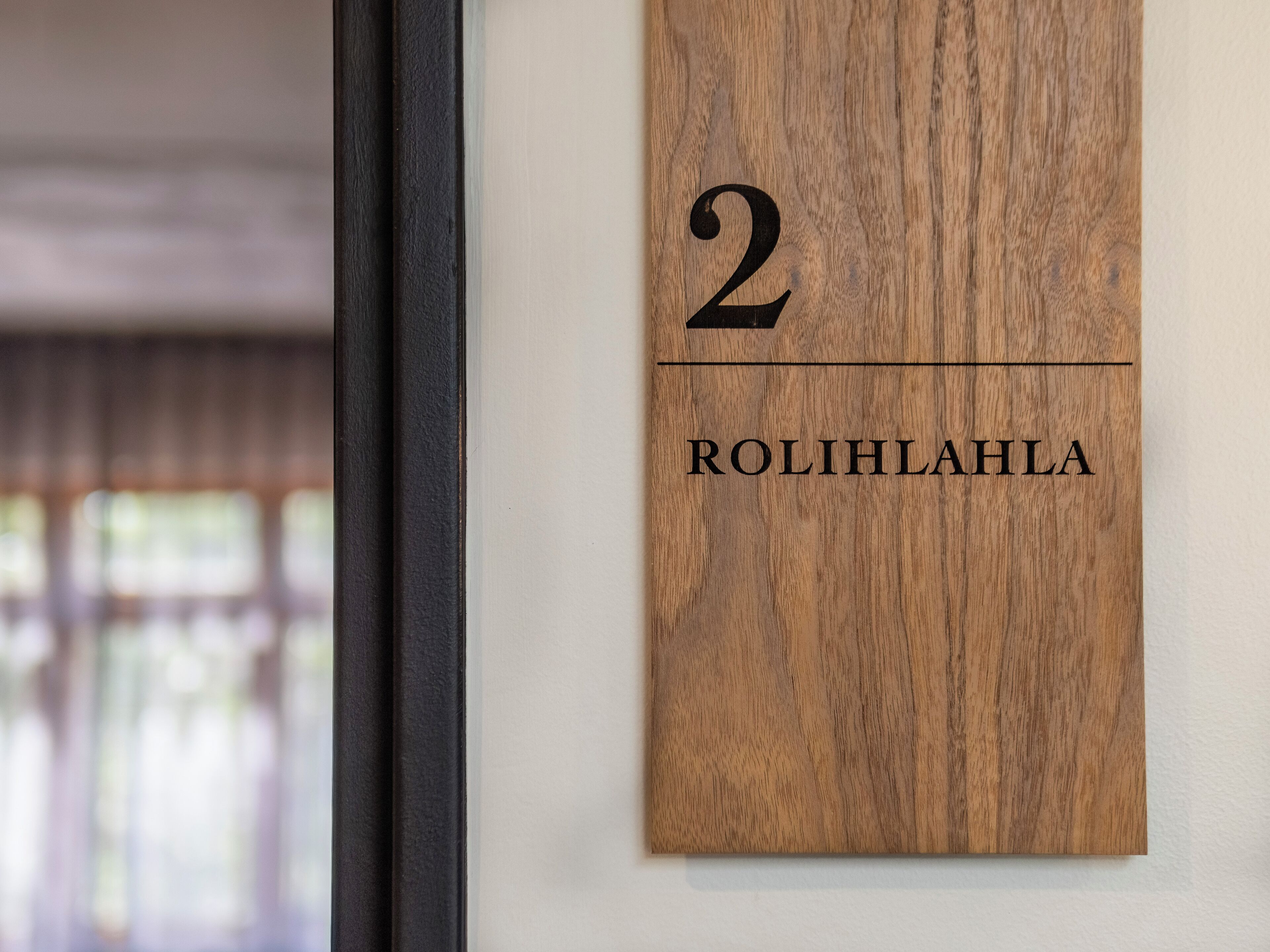 Una placa de madera con el número 2 y el nombre 'ROLIHLAHLA' en una pared blanca.