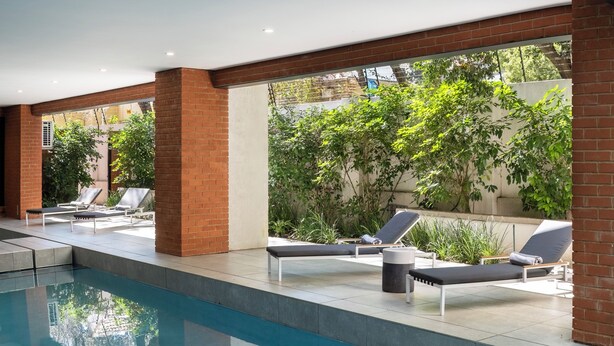 A modern indoor pool area with lounge chairs and a clear view of greenery outside.