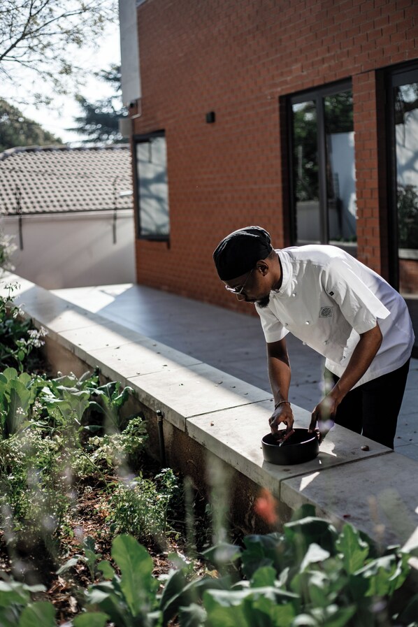 A person bending over a concrete ledge, possibly tending to plants or working with tools. - Sanctuary Mandela (Johannesburg)