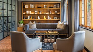 A cozy living room with a grey sofa, two armchairs, a coffee table, and a bookshelf filled with books and decorative items.