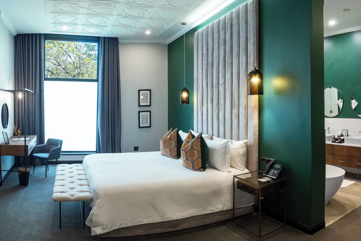 Une chambre d’hôtel moderne équipée d’un grand lit, d’un bureau, d’une chaise, d’une table de chevet avec un téléphone et d’une salle de bain avec un lavabo et un miroir.