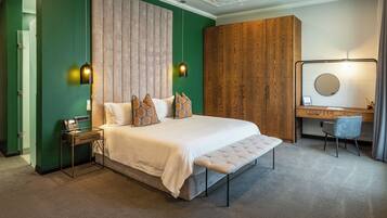 A modern hotel room with a large bed, a wooden wardrobe, a desk with a chair, and a mirror.