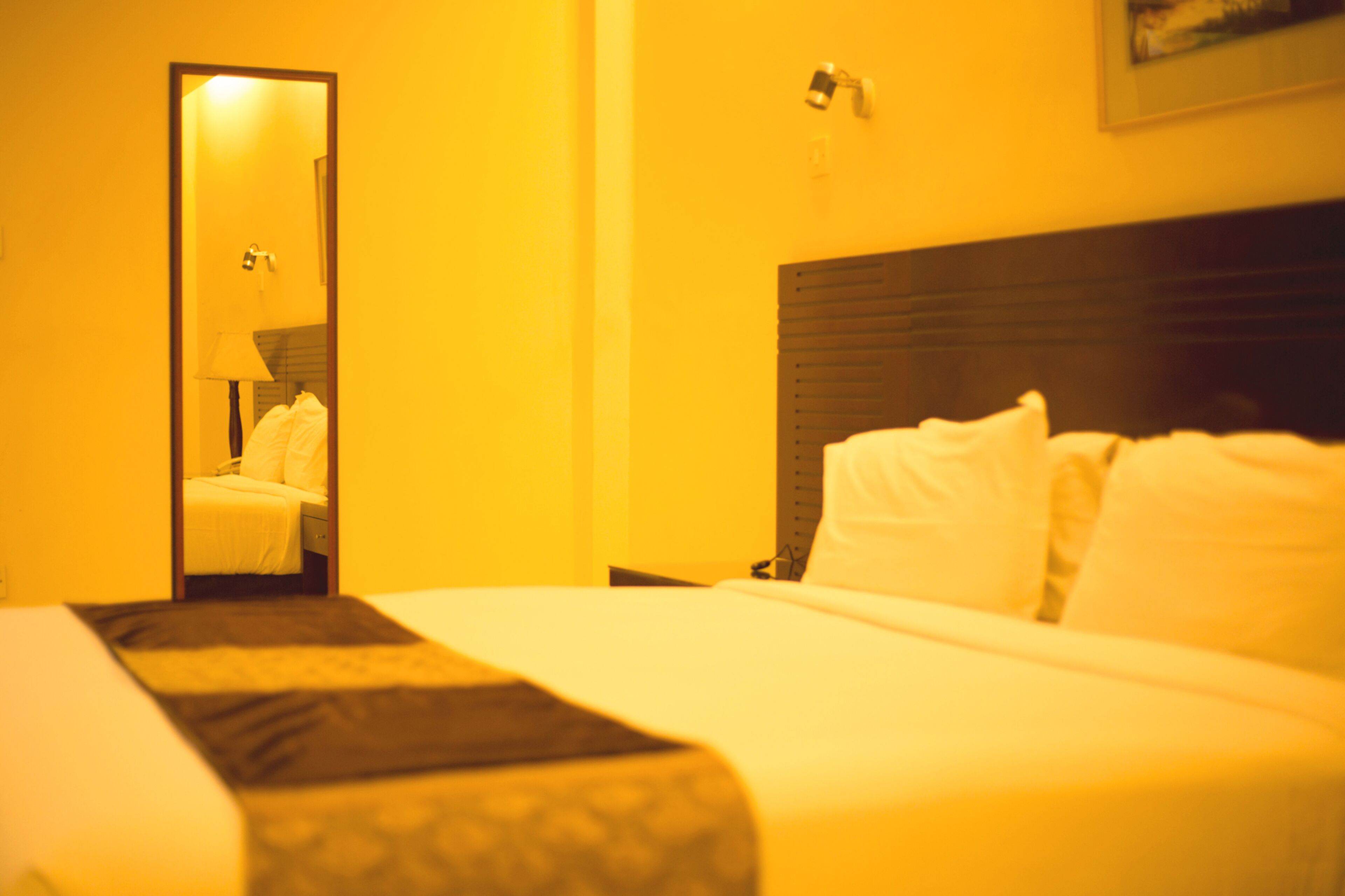 Une chambre d’hôtel avec un lit, une table de chevet, un miroir et une lampe fixée au mur.