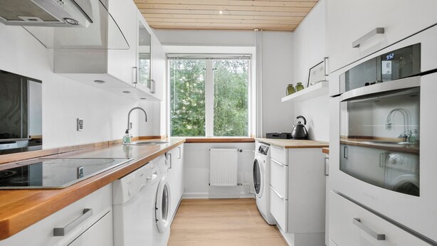 Une cuisine moderne dotée d’un plan de travail en bois, d’appareils électroménagers intégrés et d’une grande fenêtre qui laisse entrer la lumière naturelle.