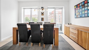 Un espace repas moderne avec une table en bois et des chaises noires, de grandes fenêtres et un tableau abstrait aux couleurs vives accroché au mur.