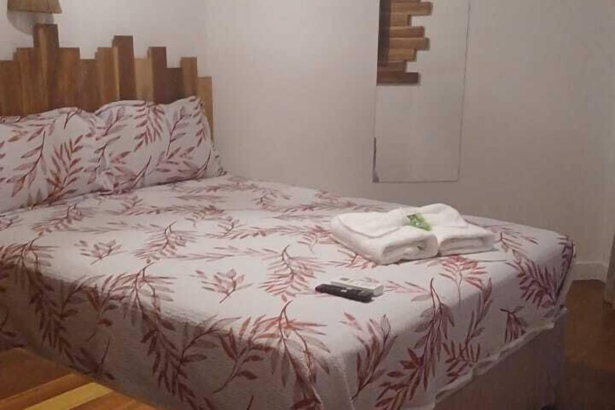A bedroom with a bed, a wooden headboard, a bedside table, a lamp, and a wall-mounted shelf.