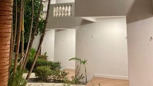A modern building with a courtyard featuring palm trees and a stone pathway. - Pousada Neptun (Conde)