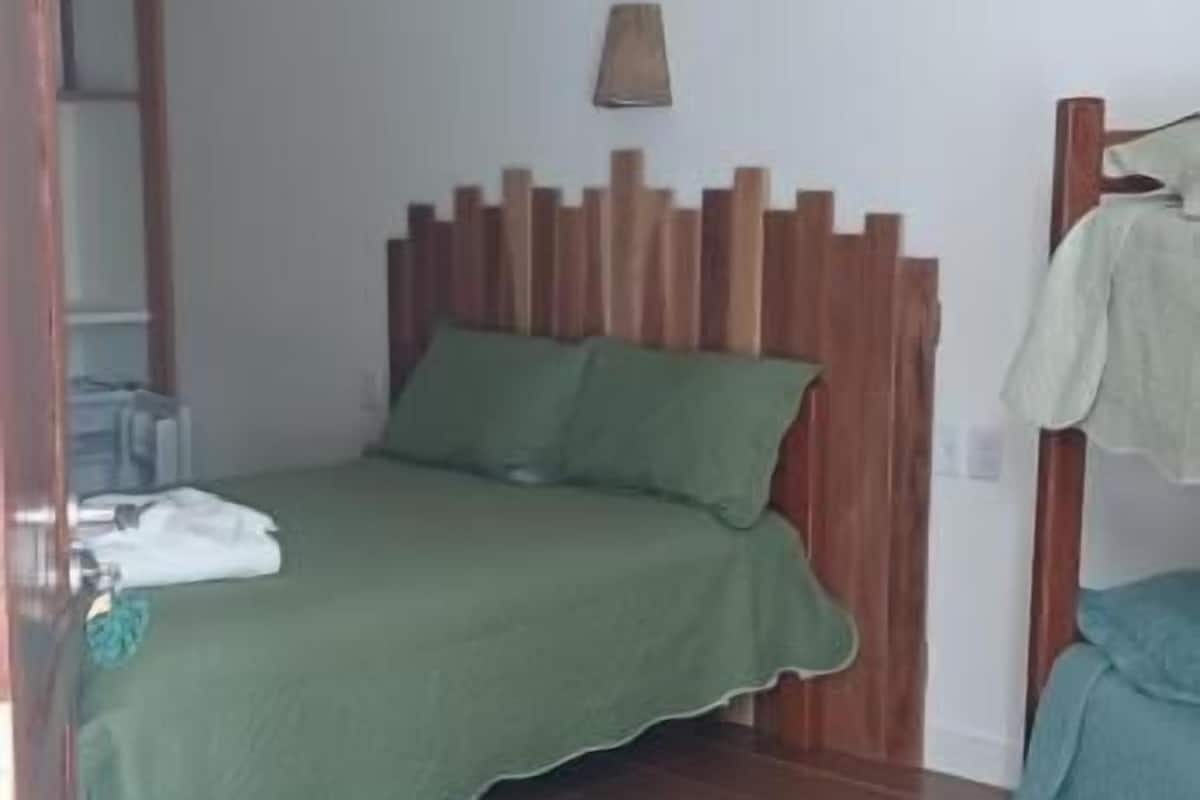 A bedroom with a wooden headboard, a green bedspread, and a hanging lamp.