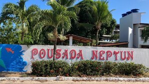 A sign for "Pousada Neptun" with a tropical backdrop, palm trees, and a building in the background. - Pousada Neptun (Conde)