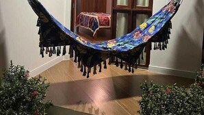 A hammock in a room with a wooden door and a window with blinds. - Pousada Neptun (Conde)
