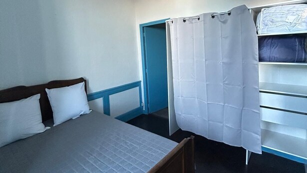 A small, single-bed room with a wooden headboard, a blue-framed door, and a white curtain.