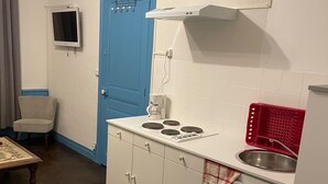 A compact kitchen with white cabinets, a blue door, a small TV, and a red basket.