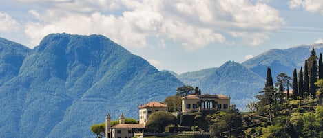 A lakeside property with a large house surrounded by lush greenery and mountains in the background.