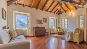 A spacious living room with wooden floors, a high ceiling, and large windows offering mountain views. - Casa Ferrari in Varenna (Varenna)
