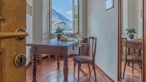 A wooden dining table with chairs, a window with a mountain view, and a potted plant on the windowsill. - Casa Ferrari in Varenna (Varenna)