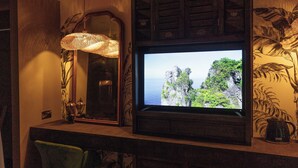 A television mounted on a wall with a tropical wallpaper, a mirror, and a wicker lamp. - The Imperial Dragon Hotel (Saundersfoot)