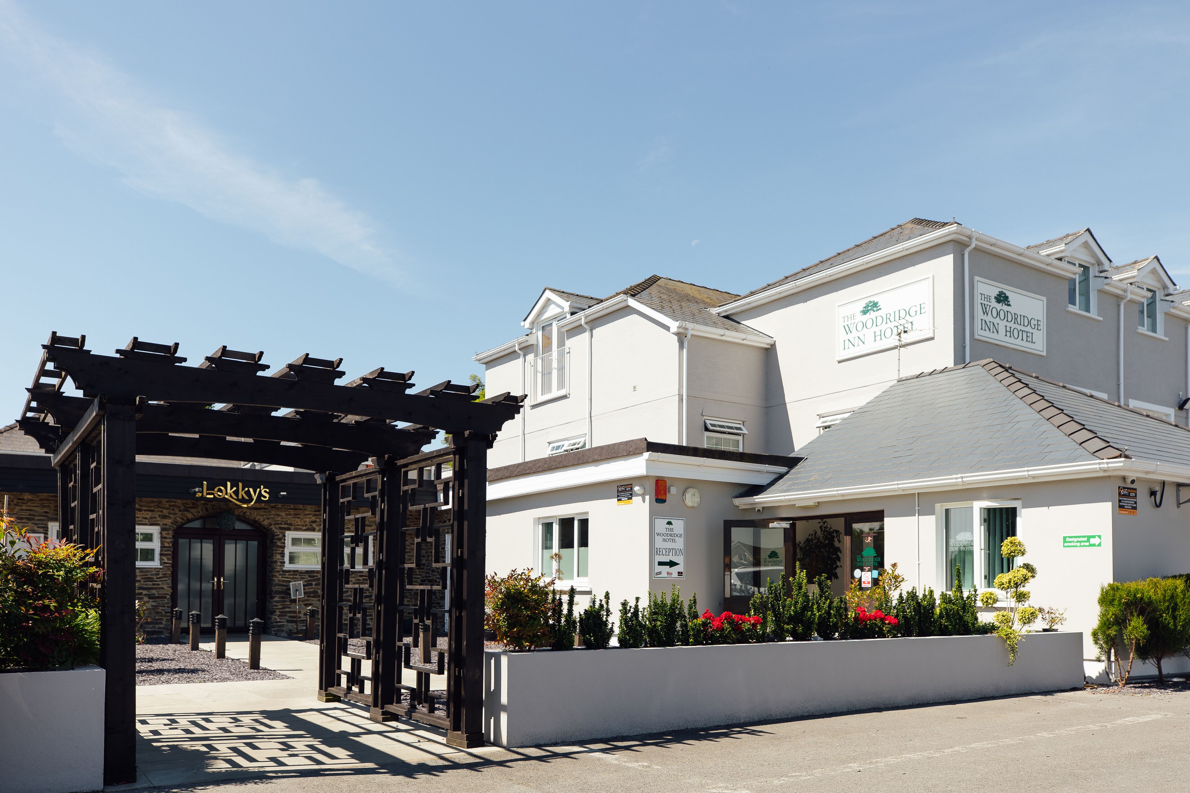 Entrada de un hotel con una zona de recepción, un cartel que dice 'The Woodridge Inn Hotel' y otro cartel para 'Lakky's' al lado.