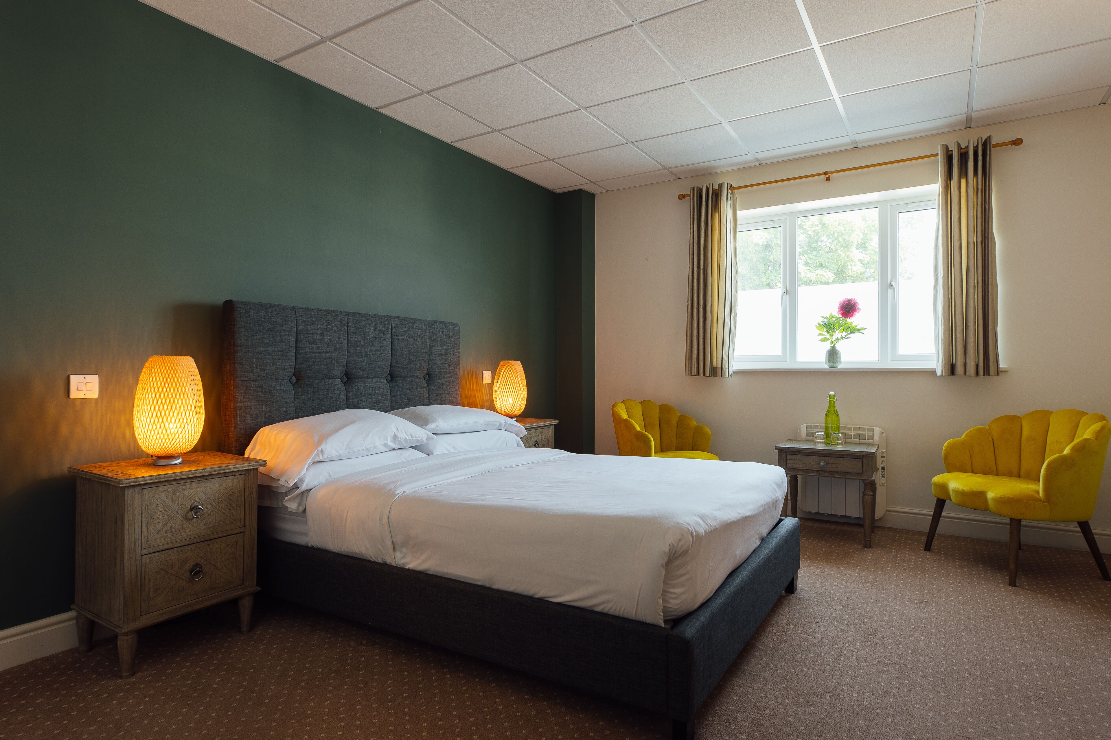 A bedroom with a bed, nightstands, a window with curtains, and two chairs.