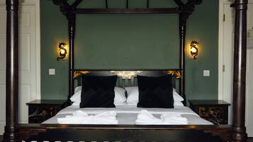 Una cama con dosel, ropa de cama blanca y almohadas negras, dos mesitas de noche y apliques con un diseño decorativo.