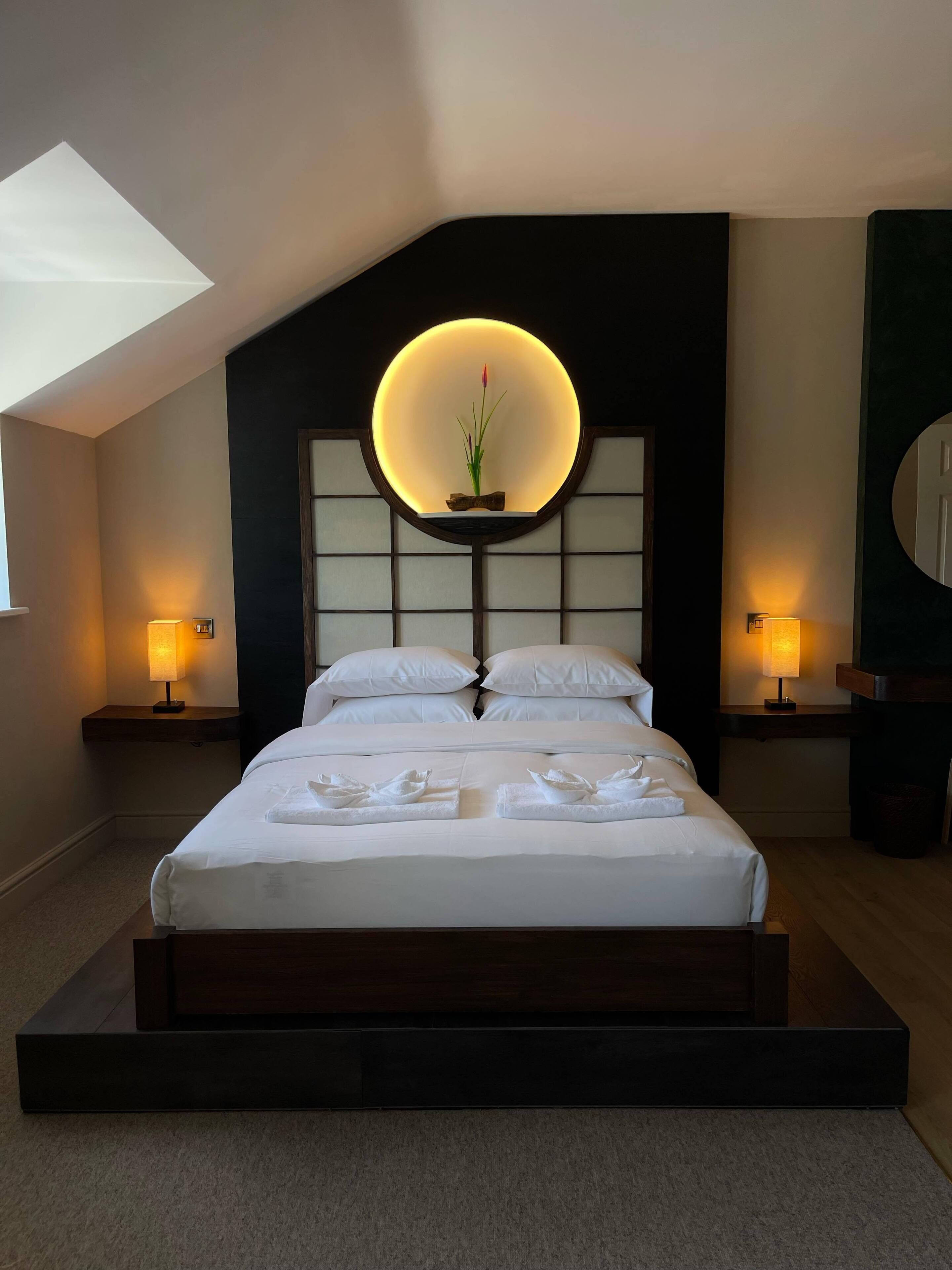 Un dormitorio moderno con una cama grande, una lámpara circular sobre el cabecero y dos lámparas de noche.