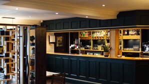 A bar area with a dark wood finish, a counter with bottles and glasses, and a seating area with a table and chairs. - The Imperial Dragon Hotel (Saundersfoot)