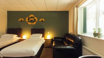 A hotel room with two beds, a leather sofa, a bedside table with a lamp, and a decorative wall piece.