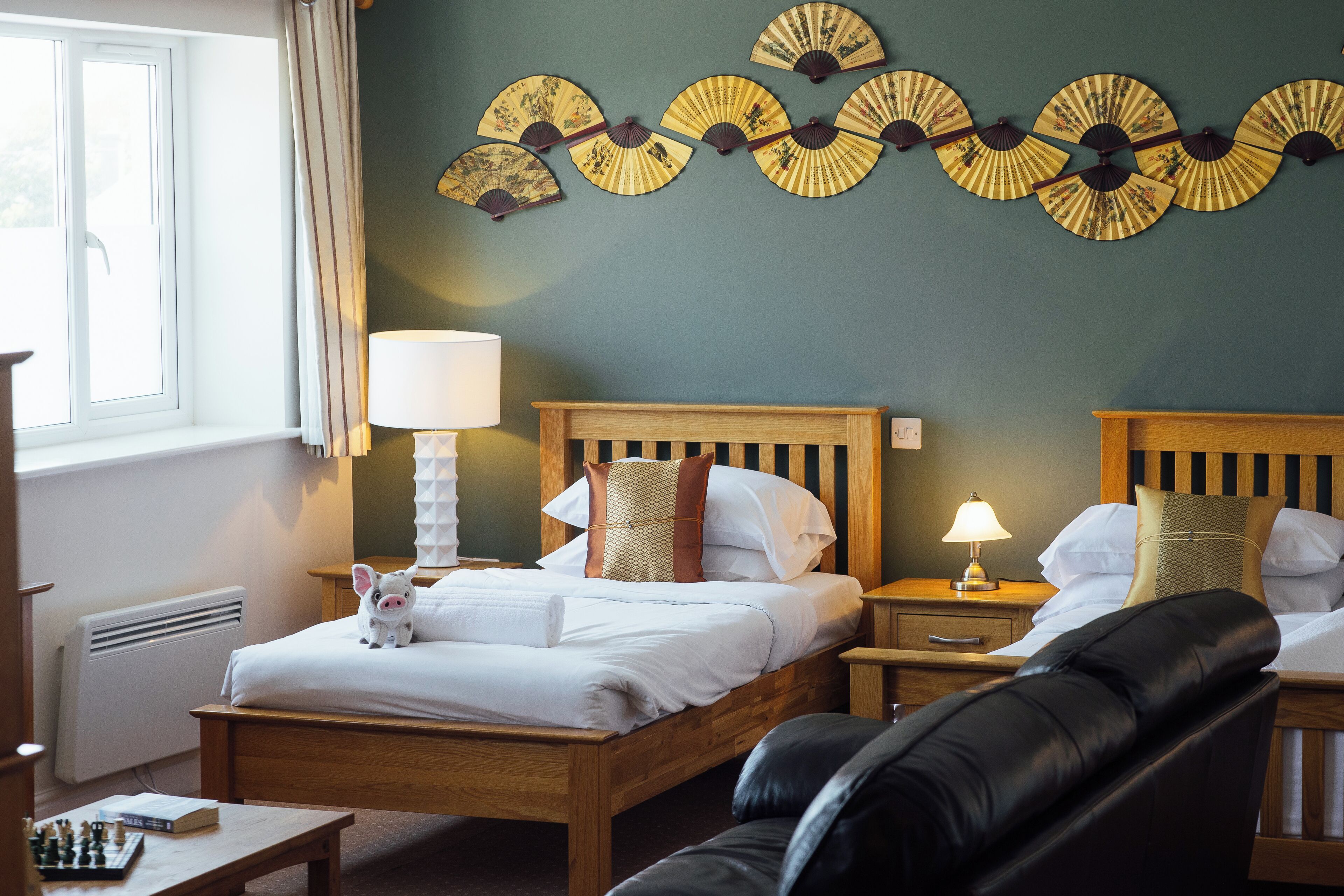 A hotel room with a wooden bed, two bedside tables with lamps, a black leather chair, and decorative wall fans.