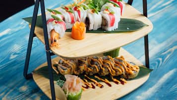 Een meerlaags houten plateau met sushi en sashimi op een blauwe houten tafel.