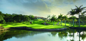 A golf course with a water body, palm trees, and a building in the background.