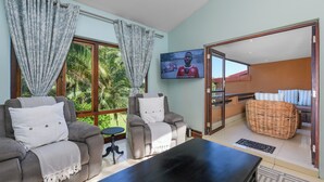 Een woonkamer met een bank, fauteuil en een flatscreen televisie aan de muur.
