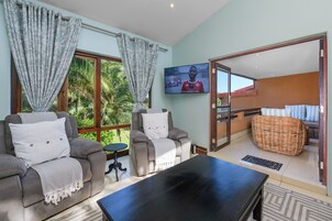 A living room with a sofa, armchair, and a flat-screen TV mounted on the wall.