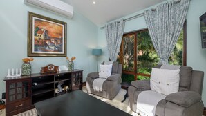 Een woonkamer met een bank, fauteuils, een salontafel, een televisie en een schilderij aan de muur.