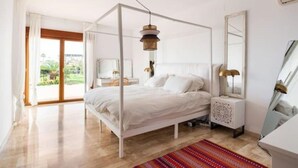 A bedroom with a four-poster bed, a nightstand with a lamp, a large mirror, and a view of the outdoors. - Villa Zebra with sea views from every room! (Benalmádena)
