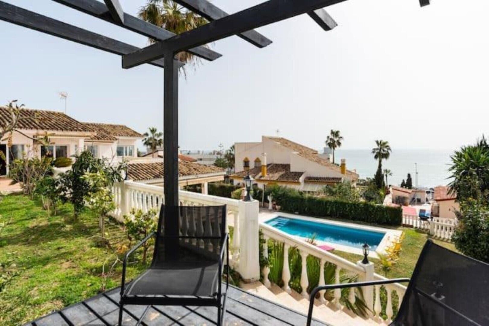 Un balcon avec une piscine, entouré de maisons et de palmiers, donnant sur une zone côtière.