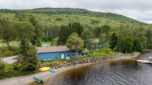 A lakeside cabin with a dock, surrounded by forested hills. - Domaine Bleu - Lakefront & Private Beach (Pohénégamook)
